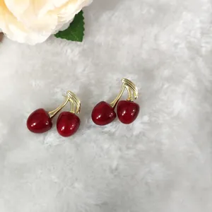 Minimalistische rote Kirschohrringe mit Goldblättern auf weichem weißem Plüsch