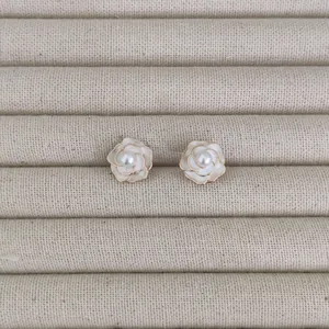 Detail of camellia earrings with white enamel petals, gold edges, and central pearl inlay