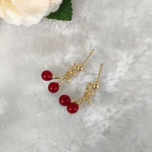 Detailansicht der Kirsch-Ohrringe mit goldenem Blatt auf weichem weißem Pelzhintergrund