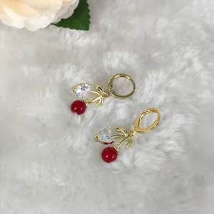 Detailansicht von Kirschohrringen mit roten Perlen, Herz-Zirkon und Goldblättern