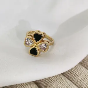 Macro detail of golden four-leaf clover ring with black enamel and white heart-shaped stones
