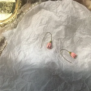 Detailed close-up of pink tulip earrings with gold hooks on a romantic textured backdrop