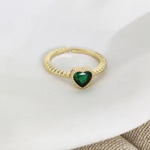 Close-up of golden beaded ring featuring a heart-shaped green stone on white fabric