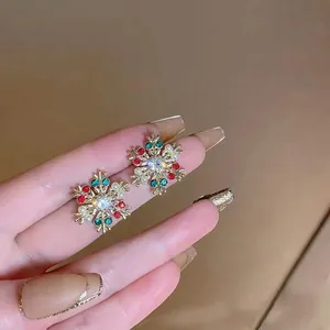 Golden Christmas snowflake earrings with red green rhinestones and white pearls on fingers
