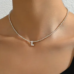 Detailaufnahme der Perlenkette mit einem silbernen Buchstaben L Anhänger am Hals