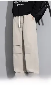 Detail of beige cargo pants featuring long white drawstrings and patchwork on knees