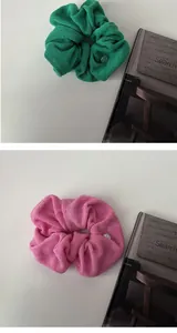 Detail view of plush green and pink scrunchies with elegant gold metal tag accents