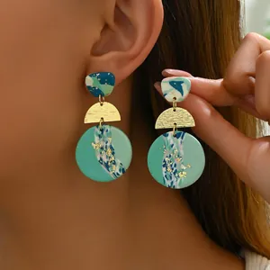 Detailed macro view of handmade geometric acrylic earrings with gold leaf and green marble texture
