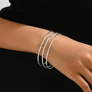 Dettaglio di tre braccialetti argentati testurizzati con finitura sfaccettata brillante