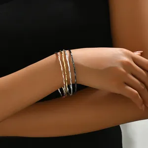 Dettaglio di quattro bracciali rigidi in metallo con trama diamantata lucida su modella
