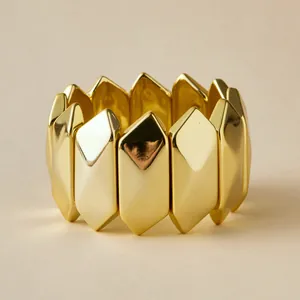 Detalle de una pulsera elástica dorada estilo bambú con eslabones metálicos pulidos