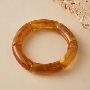 Détail macro de tubes courbés en acrylique ambre avec texture marbrée sur bracelet élastique