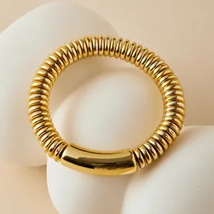 Brazalete bohemio dorado con diseño de bambú curvo sobre fondo de piedra minimalista