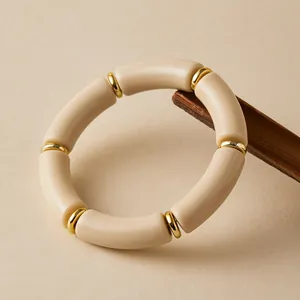 Dettaglio di un bracciale bohémien in acrilico crema con distanziali dorati su legno