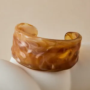 Bracelet manchette en résine ambrée à texture ondulée sur un support minimaliste