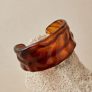 Détail macro d'un bracelet manchette en acrylique ambré avec texture ondulée irrégulière