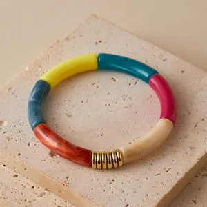 Detailed macro view of colorful resin tube beads with gold metal ring accents on a stone surface