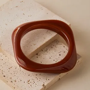 Detail of reddish-brown irregular square resin bangle on a beige stone surface