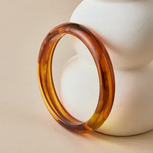 Close-up of bohemian amber resin bangle with retro tortoiseshell texture on beige surface