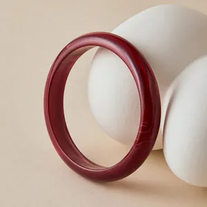 Close-up of deep red acrylic bangle with polished finish on a ceramic prop