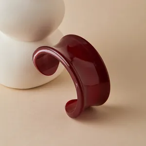 Close-up of deep red acrylic cuff bracelet with marble texture on white ceramic stand