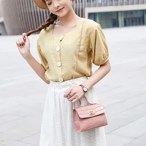 Sac bandoulière rose à motif crocodile avec chaîne dorée porté par un mannequin femme