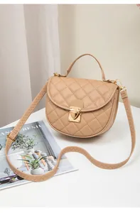 Detail of beige quilted saddle bag featuring golden metal clasp and handle on table