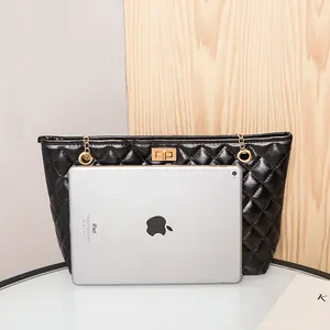 Black quilted tote bag with gold chain strap and clasp, shown next to iPad for size comparison