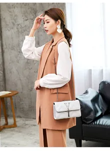 Detail view of a white quilted chain crossbody bag styled with a brown long suit vest