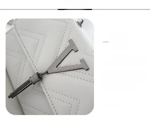 Detail of white quilted crossbody bag with gunmetal V-shaped hardware and tassel pendant