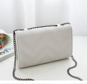 Detail of light beige quilted crossbody bag with chevron pattern and dark metal chain