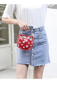 Détail d'un sac transparent en PVC avec pochette rouge à fleurs et anse dorée