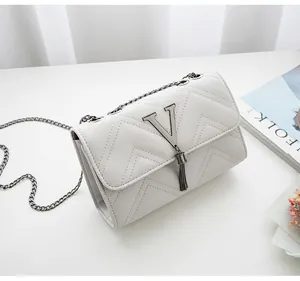 Detail of white quilted chain bag with silver V-shaped logo and elegant metal tassels