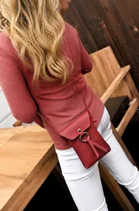 Petit sac bandoulière rouge avec anneau métallique et pompon porté par un mannequin