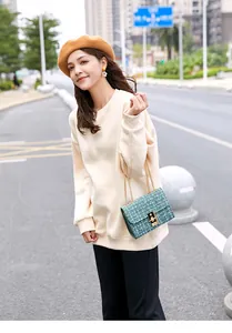 Close-up of green tweed shoulder bag with gold chain strap on a cream sweatshirt