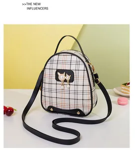 Detail view of mini plaid backpack featuring pearl cat charm and black leather straps
