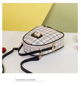 Detail of checkered crossbody bag with pearl charm and golden kitten metal accessory