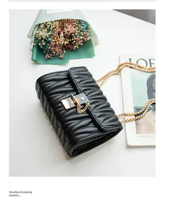 Detail of black quilted crossbody bag featuring gold chain strap and vertical metal lock
