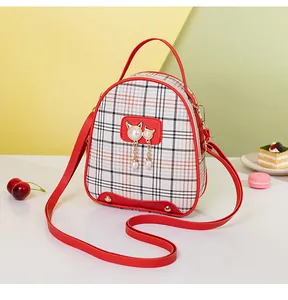 Detail of red checkered mini backpack with pearl cat pendant and sleek leather straps