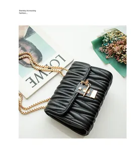 Detail of black pleated leather flap bag with square metal lock and gold chain strap