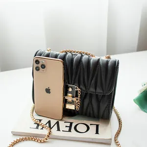 Women's black wavy quilted chain bag with gold metal lock shown beside a smartphone