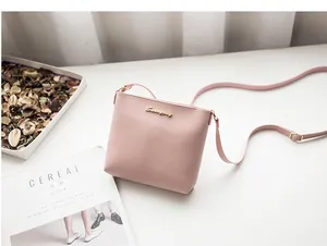 Pink leather crossbody square bag with gold metal logo and adjustable strap on a white desk