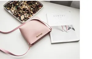 Detail view of pink crossbody bag with gold metal logo on a stylish desk setup
