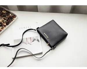Top view of a black square crossbody bag with gold metal logo on a minimalist background
