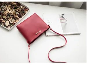 Flat lay of red minimalist PU leather crossbody bag with gold logo on white background