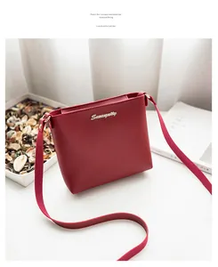 Detail of red lychee grain leather crossbody bag with golden metal logo and thin strap