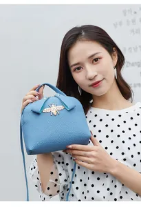 Detail of light blue lychee texture leather bag with a gold bee-shaped metal buckle