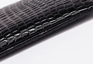 Detalle de cuero negro con patrón de cocodrilo, costuras precisas y un acabado brillante