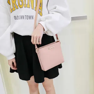 Pink minimalist crossbody square bag with golden logo worn by model in casual outfit