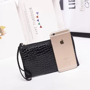 Compact black crocodile embossed clutch bag with wrist strap shown next to phone